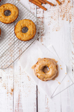 Top View of Homemade Maple-Glazed Apple-Cinnamon Doughnuts on a White Wood Table; Cinnamon Sticks and Ground Cinnamon in Background