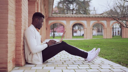 Fototapeta na wymiar Black African man working in front of laptop sitting on floor outside
