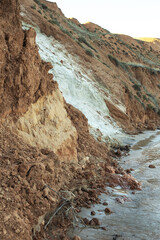 Coast landscape with white sand wall and brown layers of different clay. Sea or river coast with multicolored ground wall.