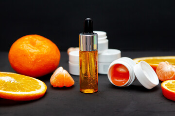 Vitamin C face skin care cosmetic concept - organic serum in a bottle and cream with natural ingredients. Tangerine and orange slices.