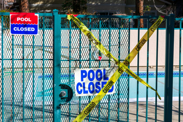 Pool closed sign on the entrance door to the pool area. Yellow barricade tape prevents accidental entrance to recreational facilities.