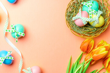 Fototapeta na wymiar Basket easter decoration: Colourful egg with tape ribbon, spring tulips, white feathers on pastel pink background. Congratulatory easter design. Top view.