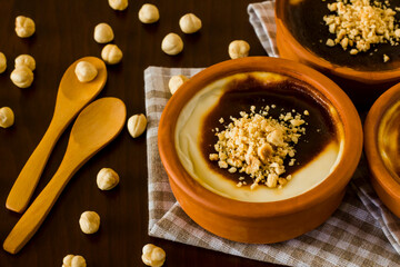 Traditional Turkish Style Baked Rice Pudding in casserole,clay dessert bowls,on wooden table with nuts and spoons
