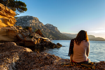 A young and beautiful girl dressed in casual clothes looking at the sunset at a beautiful beach in Artà Mallorca Balearic Islands Spain with a impressive view of the sea and the Tramuntana mountains