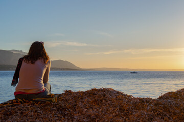 A young and beautiful girl dressed in casual clothes looking at the sunset at a beautiful beach in Artà Mallorca Balearic Islands Spain with a impressive view of the sea and the Tramuntana mountains