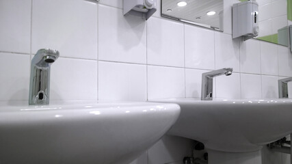 Pattern of modern white bathroom sink and faucet in public toilet and restroom. Touchless taps. Virus protection concept. Sanitary rules and requirements. Contemporary washroom and wc. Safe hygiene.
