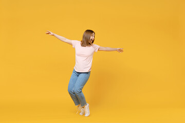 Full length of young caucasian student woman 20s wearing casual basic pastel pink t-shirt, jeans standing on toes dancing leaning back have fun isolated on yellow color background studio portrait.