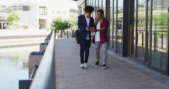 Two diverse male friends walking in the street using a digital tablet