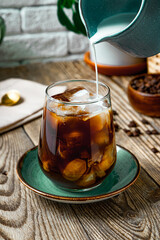  Cream is poured into a glass of iced coffee, vertical photo