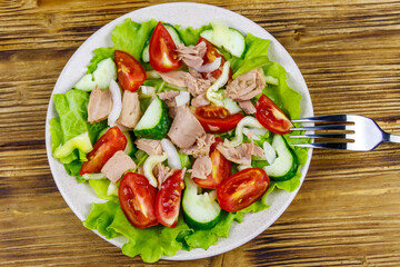 Tasty tuna salad with lettuce and fresh vegetables on wooden table. Top view