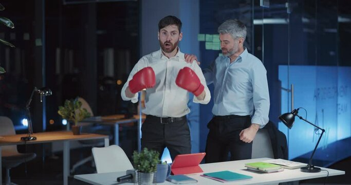 Indoor portrait couple of caucasian bearded drunk funny businessmen wearing boxing gloves punching at camera asking for competitive challenge.