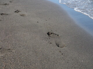 foot prints on a black sand beach with tilt-shift blur. Surf in background.