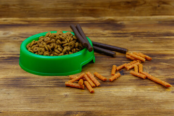 Dog delicacy food and feed in green plastic bowl on wooden background. Dog care concept