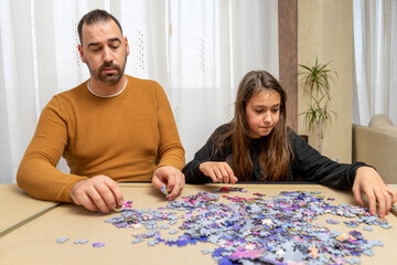Concentrated father and daughter trying to put together a complicated puzzle of small pieces