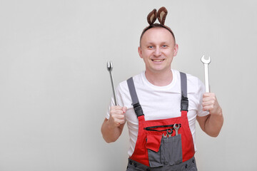 Easter holiday, celebration concept. funny smiling engineer worker or mechanic is wearing rabbit ears on head and holding wrenches white background. celebrating orthodox day