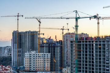 Fototapeta na wymiar Construction site, cranes and multi-storey unfinished buildings at sunrise or sunset in winter
