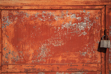 old rusty door with a padlock, fragment of a terracotta iron door with a lock, cracked paint on metal