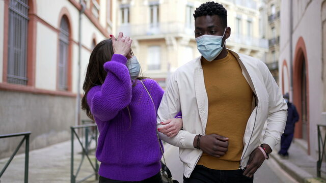 Interracial diverse couple wearing covid-19 face masks walking outside in street.