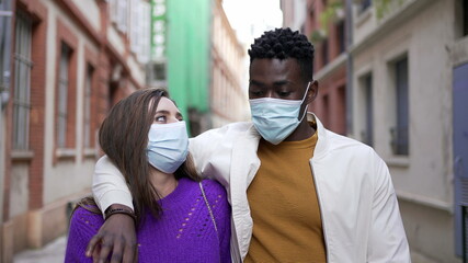 Interracial diverse couple wearing covid-19 face masks walking outside in street.