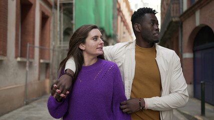 Interracial young couple walking together in city street. Black man arm around girlfriend