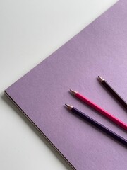 Colored pencils on purple paper album on white table. Artist, art and hobby. Drawing and painting