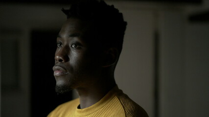 Pensive black African man standing by window, close-up face thinking