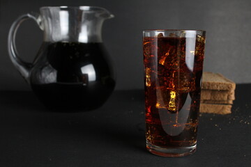 Dark bread kvass poured into a glass with solder and stands in a jug on a gray black background with a place for text and copyspace