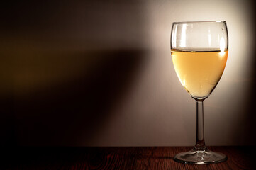 The glass with wine stands on a wooden shelf. Light falls on it.