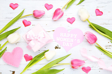 Tulip flowers, card with text Happy Womens Day, gift box, ribbon and hearts on white wooden background