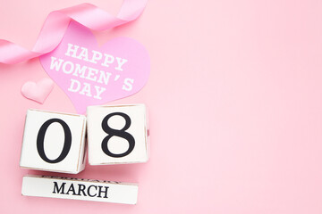 Card in shape of heart with text Happy Womens Day, wooden cube calendar and ribbon on pink background