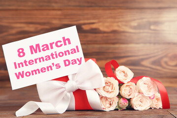 Rose flowers, gift box and card with text 8 March International Womens Day on brown wooden background