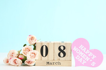 Rose flowers, card in shape of heart with text Happy Womens Day and wooden cube calendar on blue background
