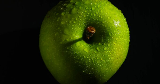 A green apple rotating on a black background, top view