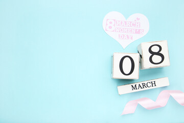 Card in shape of heart with text 8 March Womens Day, ribbon and white cube calendar on blue background