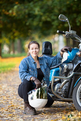 Female motorcycle rider with white crash helmet in hand sitting near her blue bike