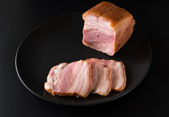 Food, a piece of bacon and cut into slices, on a black plate on a black background