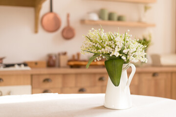 Bouquet of spring fragrant flowers of lilies of the valley in a vase on the kitchen table. Light...