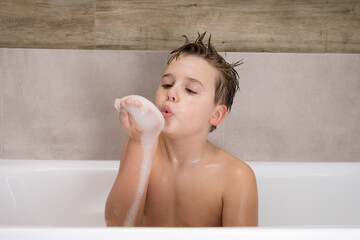 Funny boy playing with water and foam in a bathroom Cute happy child bathe at home healthy childhood