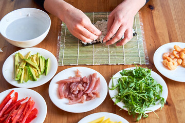 young woman prepares sushi with fresh ingredients at home. on wooden table.