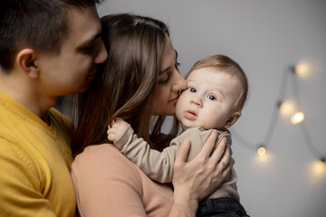 Happy young family, mom kisses little son, father hugs baby