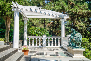 Gazebo with old bronze statue of Cupid & lion. Blooming plants all around. Shot in city park of Aivazovsky, Partenit, Crimea