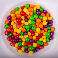 Top view of a pile of colorful shiny Skittles in a white round bowl
