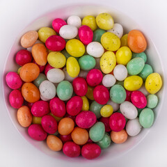 Top view of a pile of colorful shiny Easter eggs in a white round bowl
