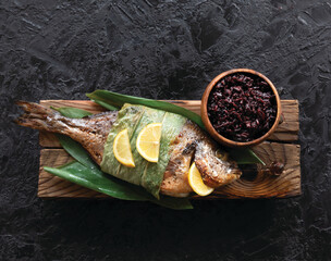 grilled dorada fish in bamboo leaves and black rice. Top view