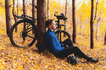 Stress relief activities, simple pleasures and workout outdoor. Tired cyclist is sitting on fall leaves in forest and resting. Togetherness with nature