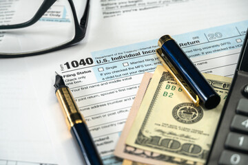 Tax form lies near dollar bills and pen, calculator, glasses . Income tax return time