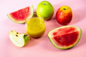 Many fruits and glass of smoothie drink in arrangement on pink.