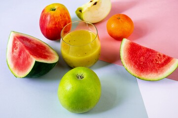 Many fruits and glass of smoothie drink on pastel color background.