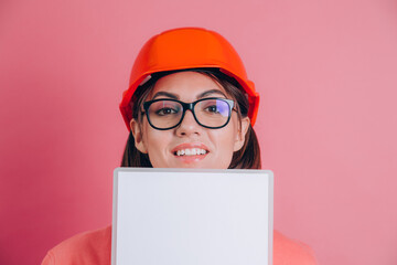 Smiling woman worker builder hold white sign board blank against pink background. Building helmet.