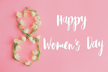 Happy womens day greeting card, 8 march. Stylish handwritten text sign on spring flowers in 8 shape on pink paper flat lay. International womens day